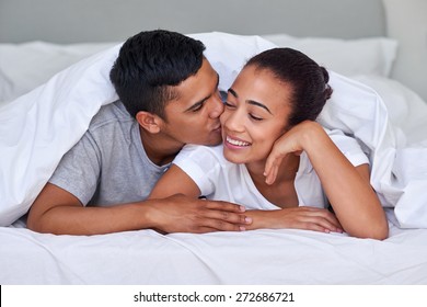 romantic young affectionate married couple kissing on bed under duvet at home