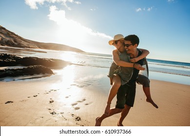 Romantic young couple enjoying summer holidays. Handsome young man giving piggyback ride to girlfriend on beach.