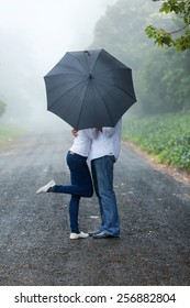 Romantic Young Couple Hiding Behind The Umbrella In The Rain