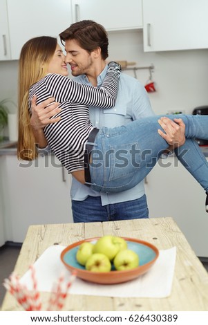 Romantic young couple kissing in the kitchen as the young man carries his wife in his arms