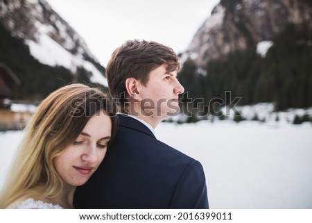 Romantic young couple looking away, back view, lake and winter mountains on background