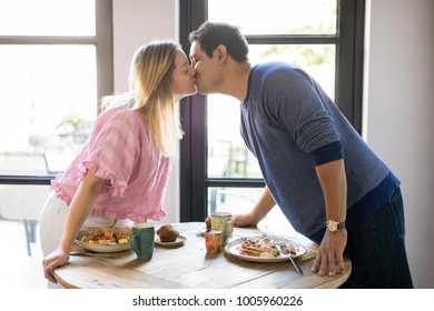 Romantic Young Couple In Love Reaching Across The Table And Kissing At Restaurant