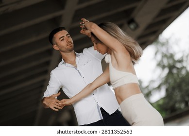 Romantic young couple practicing partner dance beneath an overpass, showing movement, trust and connection.