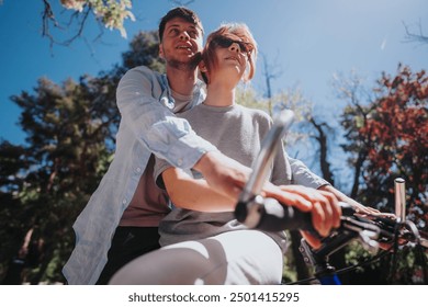 Romantic young couple share a tender moment while riding bikes in a park under clear blue skies, surrounded by trees. - Powered by Shutterstock