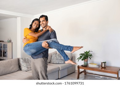 Romantic Young Middle Eastern Man Lifting Woman. Joyful Couple Moving Into Their New Home With Husband Carrying His Wife. Man Carrying Indian Woman In His Arms Moving In Booking House For Vacation.