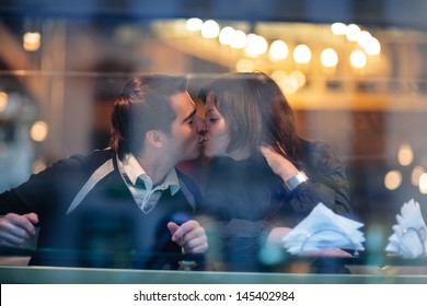 Romantic young valentine couple in love kissing in cafe. Candid view through window glass.
