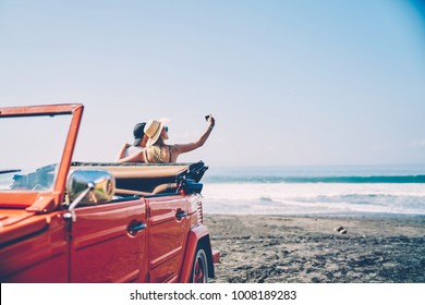 Romantica couple making photo on smartphone camera standing near vintage rental car on ocean beach enjoying summer vacation together, hipsters taking picture on cellular resting near sea on weekends - Powered by Shutterstock