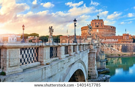 Rome, Italy. Bridge with angels and demons statue in front of Castle of the Holy Angel (Castel Sant Angelo) during evening sunset. Famous touristic landmark. Statues and street lamps medieval.