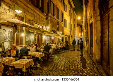 Rome, Italy - June 18, 2014. A Residential Street In Rome, Where People Are Dining Outdoors At A Small Neighborhood Restaurant On An Old Cobblestone Street At Night.