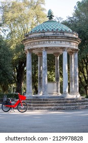 Rome, Italy - October 10, 2020: Neoclassical Small Circular Temple Of Diana (Tempietto Di Diana) In Villa Borghese Gardens, Red Bicycle Red Bicycle Standing Next To It