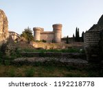 Rome ruins of antique walls of the amphitheatre in Italian town. Towers of medieval castle Rocca Pia in Tivoli in evening light.