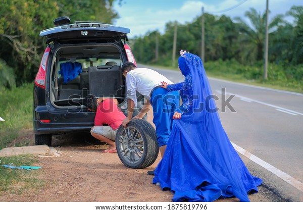 Rompin, Malaysia -\
Novemberth , 2020 : Unexpected problems on the outdoor  wedding\
session photography. Just married series. Man changing a flat tyre\
after vehicle\
breakdown.