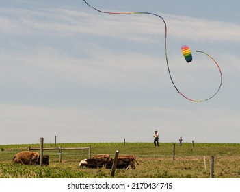 Ronks, Pennsylvania, June 19, 2022- Amish Man Flying A Colorful Rainbow Kite On Sunday Summer Afternoon With Small Child Watching