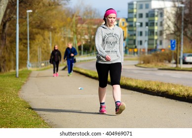 Ronneby, Sweden - April 3, 2016: Young Adult Woman Power Walking On A Pedestrian Walkway In Town. She Wears Earphones And Looks Concentrated.