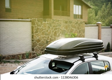 Roof Of The Car With A Black Cargo Box On The Hooks Near The Country House In The Evening.