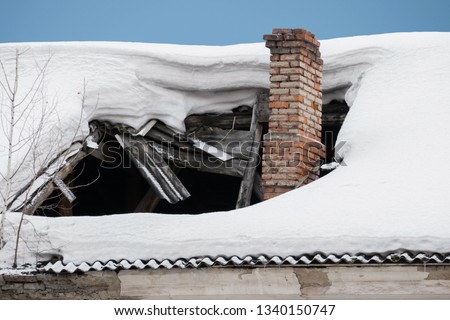 The roof collapsed under the weight of snow. Damaged falling roof and chimney on sunny day with clear blue sky. 