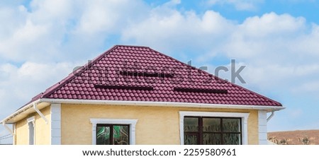 The roof of a cottage with a metal coating, snow guards, a chimney, against the background of a blue sky. Inclined roof of a residential building made of metal profiled sheet, metal slate.