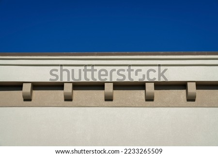 Roof eaves with dentils close-up at Destin, Florida. Beige building exterior in a low angle view against the clear blue sky at the top.
