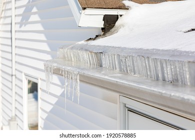 Roof Gutter Full Of Ice And Icicles After Winter Storm. Concept Of Roof Damage, Home Maintenance And Repair.