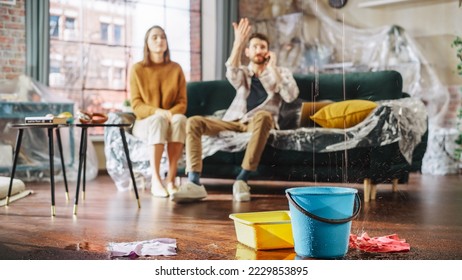 Roof is Leaking, Pipe Rupture at Home: Water Drips into Buckets in Living Room. Angry Couple in Background Calling Insurance Company, Screaming into Phone in Frustration, Trying to Find Plumber - Shutterstock ID 2229853895