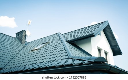 Dach eines neuen Hauses. Keramischer Kamin, Dachziegel aus Metall, Rinnen, Dachfenster. Fernsehantennen am Schornstein. Einfamilienhaus.