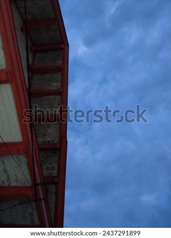The roof of an old post office building with an orange plinth is photographed from below against a grayish blue sky background
