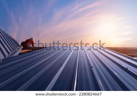 Roof repair, Construction worker installing new roof, roofing tools, power drill used on new roof with sheet metal. Roofing - construction worker standing on a roof covering it with metal.
