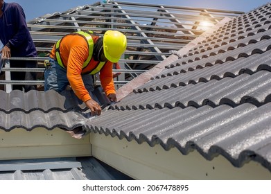 Roof repair, worker  replacing gray tiles or shingles on house with blue sky as background and copy space, Roofing - construction worker standing on a roof covering it with tiles.