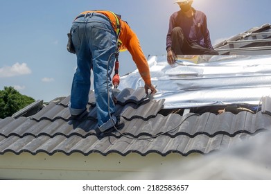 Roof repair, worker replacing gray tiles or shingles on house with blue sky as background and copy space, Roofing - construction worker standing on a roof covering it with tiles. - Shutterstock ID 2182583657