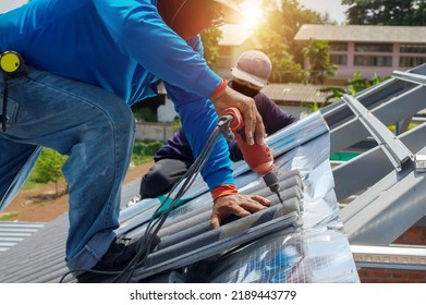 Roof repair, worker replacing gray tiles or shingles on house with blue sky as background and copy space, Roofing - construction worker standing on a roof covering it with tiles. - Shutterstock ID 2189443779
