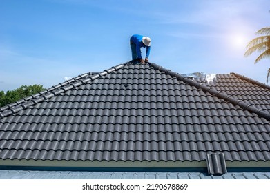 Roof repair, worker replacing gray tiles or shingles on house with blue sky as background and copy space, Roofing - construction worker standing on a roof covering it with tiles. - Shutterstock ID 2190678869