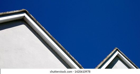 Roof and roofline against a deep blue background with no clouds in sky, white render on building facade with edges of grey roof tiles on a bright day in an abstract form.