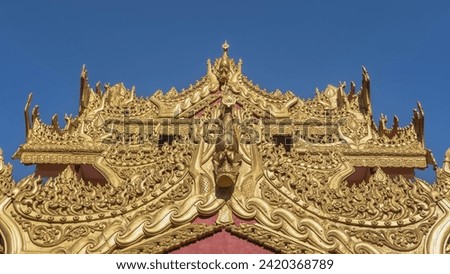 The roof of the temple is painted in gold and decorated with elegant carved ornaments, figures of gods. Close-up against a clear blue sky. Malaysia. Penang. Burmese Buddhist Temple