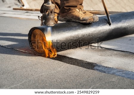 Roofer Applying Torch-On Bitumen Membrane for Waterproofing Flat Roofs in Construction and Maintenance Work