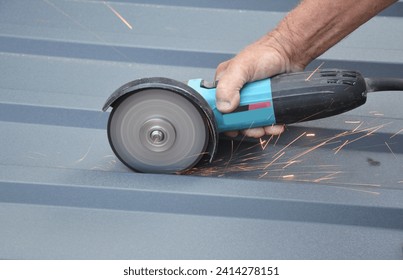 Roofer constuctor is cutting with a power angle grinder a corrugated metal roofing sheet. Cutting metal roof tile. - Powered by Shutterstock