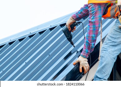 Roofer with electric drill used on new roofs with Metal Sheet on top roof at the building under construction.