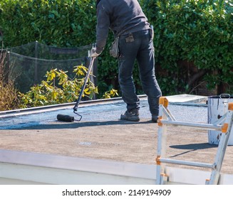 Roofer Rolls A Tar Sheet With Bitumen On A Flat Roof