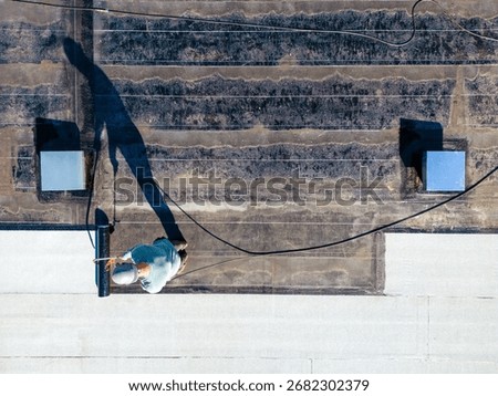 A roofer torches a membrane layer on a flat roof using a tiger torch to seal the asphalt bitumen, ensuring a durable waterproof layer.