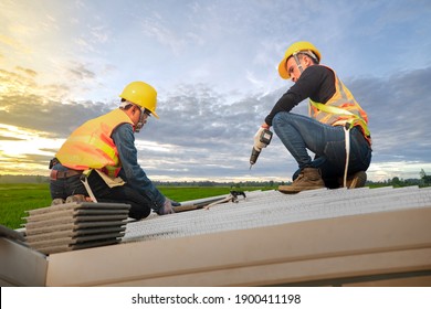 Roofer wearing safety harness belt during working on roof structure of building on construction site,Construction worker using air or pneumatic nail gun and installing concrete roof tile on top roof.