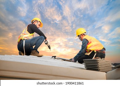 Roofer wearing safety harness belt during working on roof structure of building on construction site,Construction worker using air or pneumatic nail gun and installing concrete roof tile on top roof.