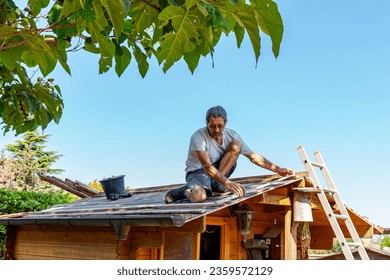 Roofer at work, installing clay roof tiles. back garden with shed, summer house garden timber outbuilding. new roof of the shed in the back yard. install tile on roof of old house.  - Powered by Shutterstock