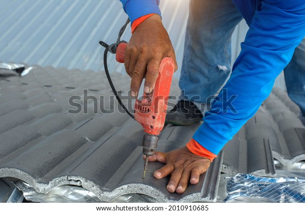 Roofer at work,\
installing clay roof tiles,Construction roofer installing roof\
tiles at house building\
site