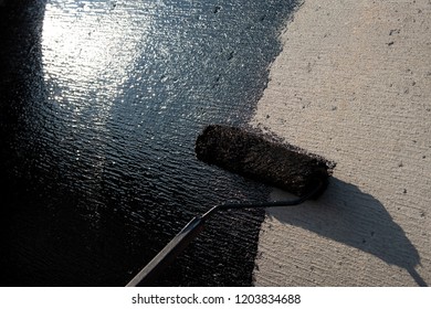 Roofer worker painting black coal tar or bitumen at concrete surface by the roller brush, A waterproofing. industrial worker on construction site laying sealant for waterproofing cement