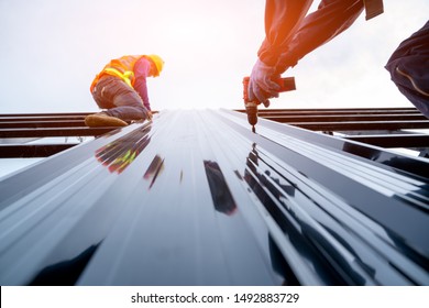 Roofer Worker In Protective Uniform Wear And Gloves, Using Air Or Pneumatic Nail Gun And Installing Asphalt Shingle On Top Of The New Roof,Concept Of Residential Building Under Construction.