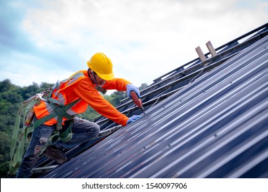 Roofer worker in protective uniform wear and gloves, using air or pneumatic nail gun and installing asphalt shingle on top of the new roof,Concept of residential building under construction.