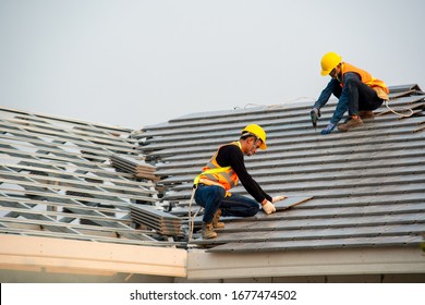 Roofer Worker In Special Protective Work Wear And Gloves,Using Pneumatic Gun And Installing Concrete Roof Tile On Top Of The New Roof,Concept Of Residential Building Under Construction.