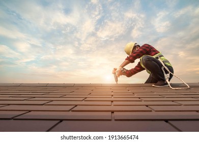 Roofer working in special protective work wear gloves, using air or pneumatic nail gun installing concrete or CPAC cement roofing tiles on top of the new roof under construction residential building