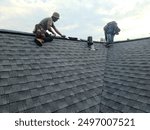 Roofers installing shingles and ridge cap on the roof of a building 