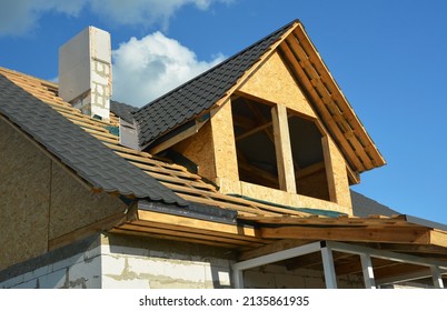 Roofing construction on the stage of metal tiles installation on a gable roof with a dormer using flashing, and unfinished brick chimney. Roofing Construction. Attic insulation. - Shutterstock ID 2135861935