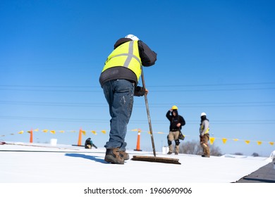 Roofing construction worker installing a flat roof. Bright blue sky in the background.